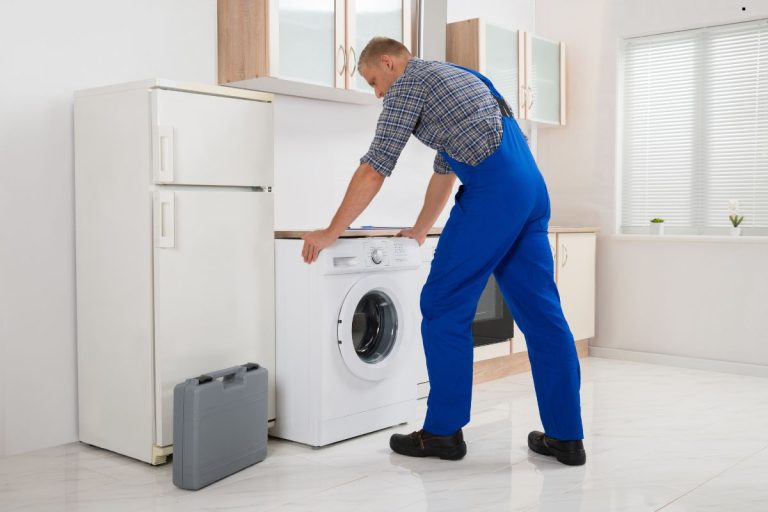 A worker in an apron loads towels into a large commercial washing machine in a clean, well-lit laundry facility.